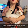 casual_clothing, chair, child, curled_cat, earrings, expressionless, floor, furniture, girl, heart_emoji, holding, home, indoor, long_hair, pet, table, television, text_overlay, white_cat, young
