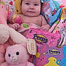 Ruby is registered to the contest to win money with this photo: baby, infant, pink_blanket, stuffed_animal, plush_toy, marshmallow_candy, peeps, packaging, smiling, cute, child, toy, soft_toy, colorful, indoors, portrait, happy, wrapped, cozy, playful