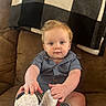 baby, blanket, blue_shirt, brown, child, comfortable, couch, curly_hair, cute, furniture, home, indoor, plaid, portrait, seated, shoe, smiling, sneaker, socks, toddler