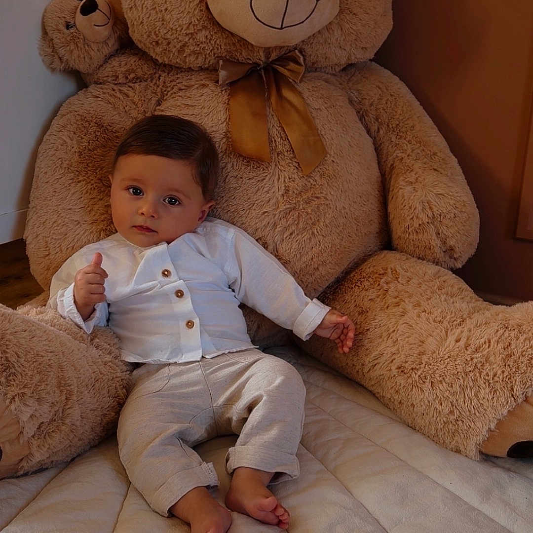 Nino participe au concours pour gagner de l'argent avec cette photo : baby, barefoot, bedspread, child, comfort, cozy, cute, furniture, indoor, pants, plush, portrait, room, smile, soft_toy, teddy_bear, thumbs_up, toy, white_shirt, young_child