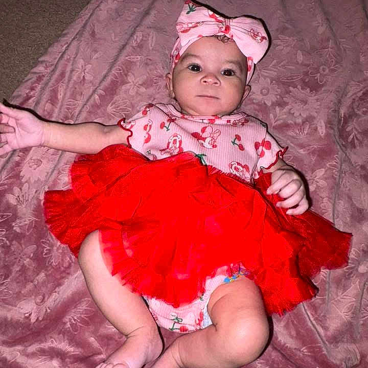 Autumn is registered to the contest to win money with this photo: baby, infant, tutu, headband, pink_blanket, red_clothing, cute, child, lying_down, soft_texture, indoors, playful, small_feet, adorable, portrait, one_person, looking_at_camera, fabric, wrapped, resting
