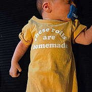 Theodore is registered to the contest to win money with this photo: baby, sleeping, pacifier, yellow_onesie, text_on_clothing, infant, child, cute, peaceful, lying_down, closeup, skin, head, arm, hand, human, indoors, soft_lighting, rest, comfort