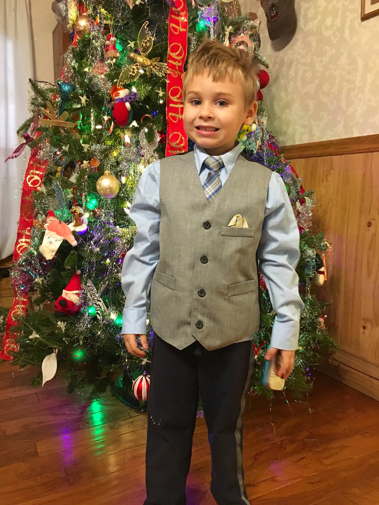 Alex is registered to the contest to win money with this photo: child, christmas, christmas_decoration, christmas_eve, christmas_ornament, christmas_tree, event, formal_wear, holiday, interior_design, joy, male, outerwear, person, plant, smile, standing, suit, toddler, tradition