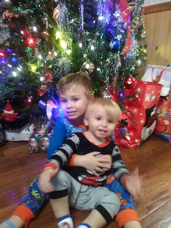 Zack is registered to the contest to win money with this photo: child, christmas, christmas_decoration, christmas_eve, christmas_ornament, christmas_tree, event, fir, holiday, interior_design, lap, person, plant, play, sitting, smile, toddler, tree