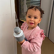 Selma a rejoint le concours — aidez-le/la à gagner de superbes lots ! casual_clothing, child, curly_hair, curtain, cute, floor, happy, holding_object, home, indoor, jeans, microphone, person, pink_sweater, smiling, standing, toddler, white_shoes, window, young_child