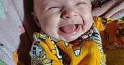 Makenzie is registered to the contest to win money with this photo: baby, smiling, laughing, yellow_clothing, cartoon_prints, blanket, infant, cute, happy, child, face, portrait, lying_down, indoors, soft_fabric, cheerful, baby_clothes, small_person, joyful, playful