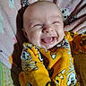 baby, baby_clothes, blanket, cartoon_prints, cheerful, child, cute, face, happy, indoors, infant, joyful, laughing, lying_down, playful, portrait, small_person, smiling, soft_fabric, yellow_clothing