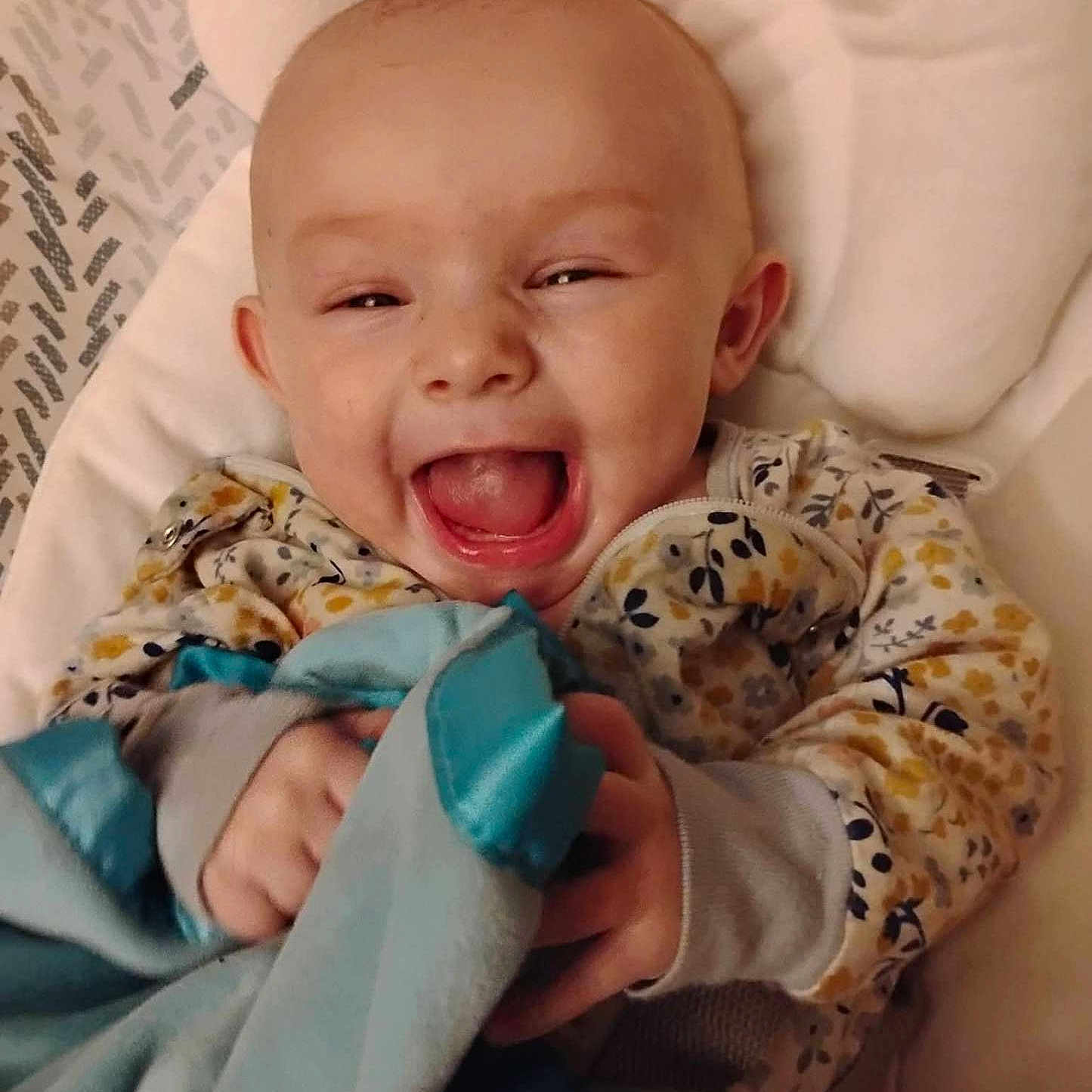 Makenzie joined the competition — help win amazing prizes! baby, smiling, blanket, floral_clothing, happy, infant, cute, child, face, portrait, hands, cozy, lying_down, soft_toy, indoors, cushion, comfort, expression, joy, closeup