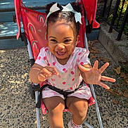 Alaia Noell joined the competition — help win amazing prizes! toddler, child, smiling, stroller, outdoor, sunlight, white_bows, curly_hair, pink_dress, sneakers, happy, reaching_hand, concrete, steps, leaves, playful, baby, person, daylight, cute