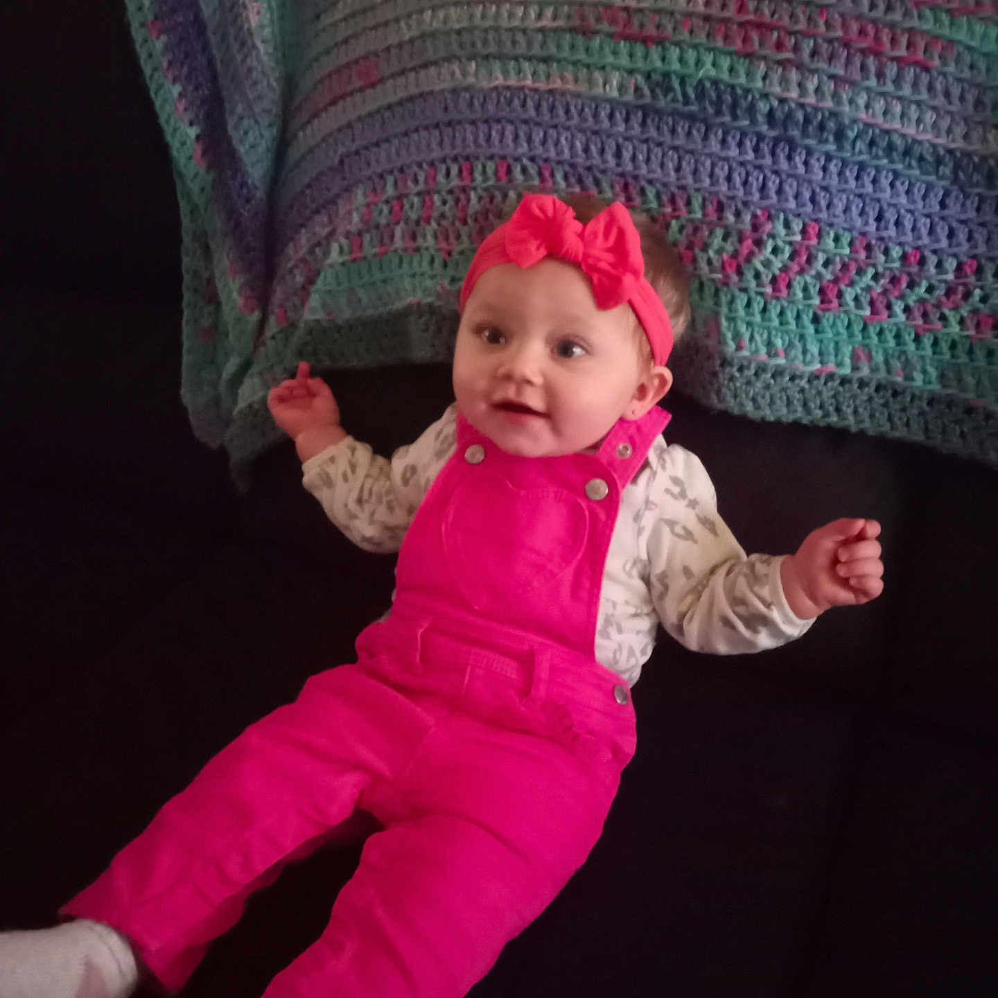 Isabella joined the competition — help win amazing prizes! baby, child, clothing, couch, cozy, cute, face, furniture, happy, headband, home, indoor, infant, knitted_blanket, person, pink_overalls, portrait, sitting, smile, young_child