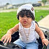 Eithan Milan is registered to the contest to win money with this photo: baby, child, curly_hair, cute, daylight, fun, gold_necklace, grass, outdoor, person, play, portrait, pout, shorts, steering_wheel, summer, tank_top, toddler, toy_car, white_beanie