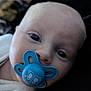 baby, pacifier, close_up, face, infant, blue, mouth, eyes, skin, head, cute, child, young, portrait, soft_lighting, indoor, sleepwear, expression, human, newborn