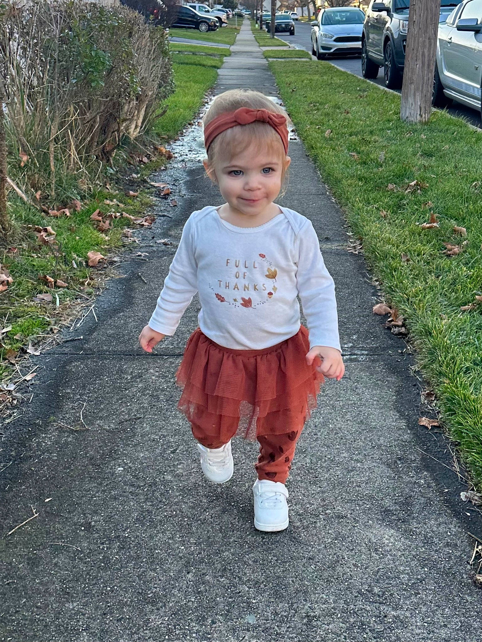 Chloe is registered to the contest to win money with this photo: asphalt, baby_toddler_clothing, car, child, driveway, fun, grass, hat, head, lawn, people_in_nature, person, plant, road_surface, sidewalk, smile, tire, toddler, tree, walking