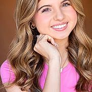 Sydney is registered to the contest to win money with this photo: portrait, smiling, young_person, female, headshot, wavy_hair, blonde, pink_shirt, earrings, makeup, white_teeth, hand_on_chin, studio_lighting, close_up, skin, necklace, model, happy, fashion, glow