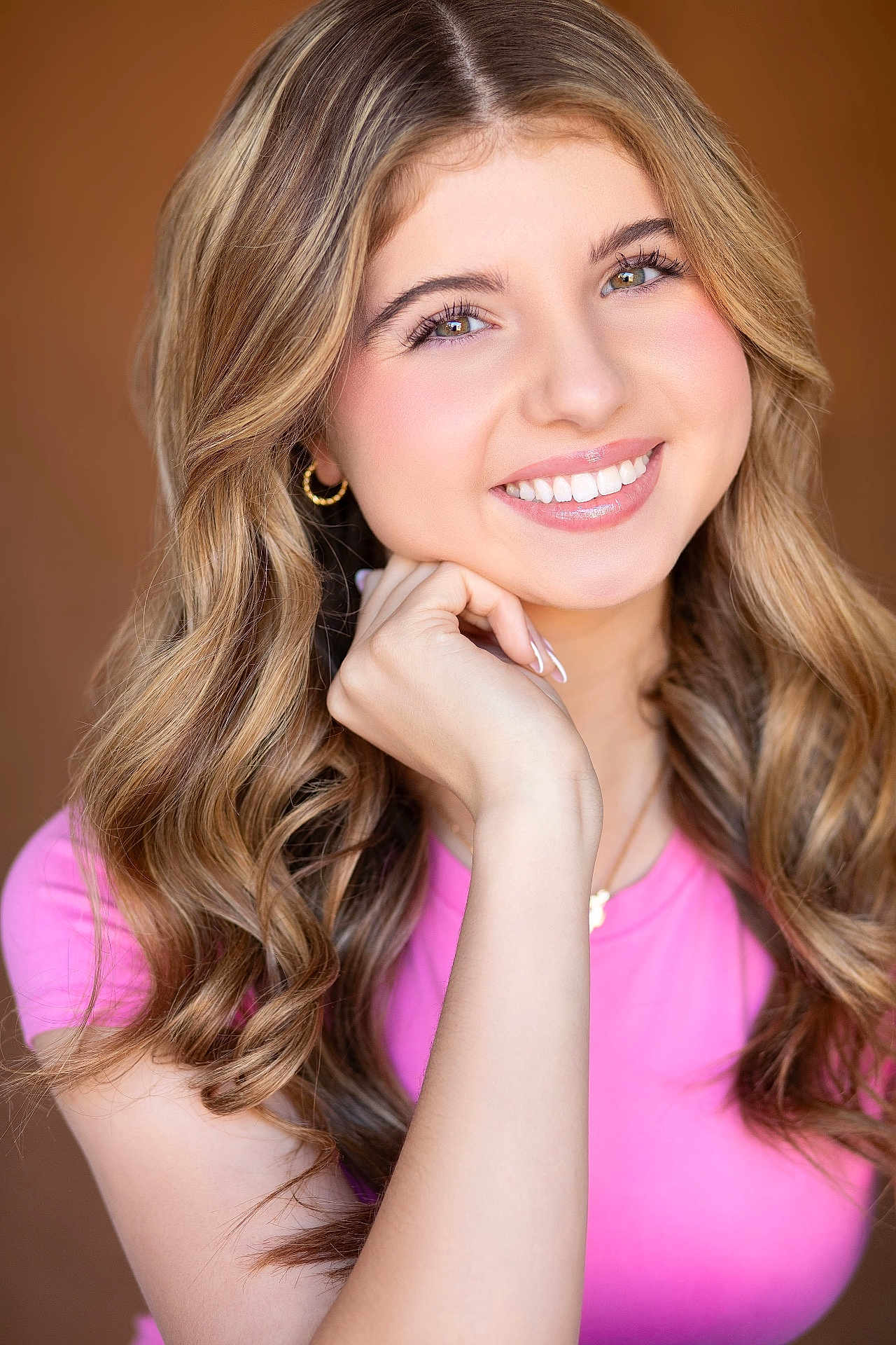 Sydney is registered to the contest to win money with this photo: portrait, smiling, young_person, female, headshot, wavy_hair, blonde, pink_shirt, earrings, makeup, white_teeth, hand_on_chin, studio_lighting, close_up, skin, necklace, model, happy, fashion, glow