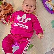 Nëyla a rejoint le concours — aidez-le/la à gagner de superbes lots ! adidas, baby, book, casual, child, cute, floor, footwear, happy, indoor, infant, lying_down, person, pink_clothing, play_mat, portrait, smiling, soft_toy, toy, tracksuit