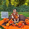 baby, infant, child, smiling, outdoor, autumn, halloween, pumpkin, flowers, orange, costume, headband, sitting, portrait, garden, grass, letter_board, seasonal_decor, blanket, happy