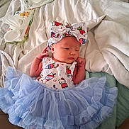 Scarlett is registered to the contest to win money with this photo: baby, infant, newborn, headband, bow, blue_tutu, dress, baby_wipes, bed, blanket, soft, cute, clothing, foot, hand, person, indoors, resting, sleepy, portrait