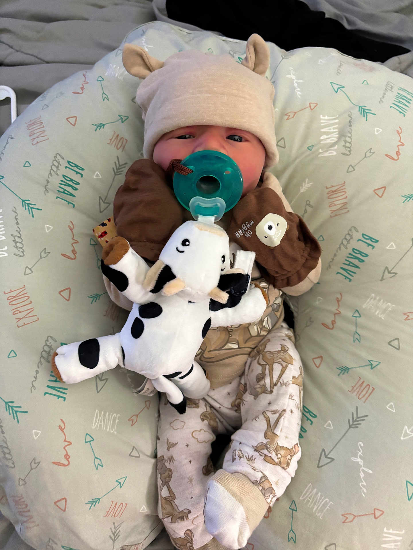 Oakley is registered to the contest to win money with this photo: baby, pacifier, plush_toy, hat, baby_clothes, cushion, pattern, animal_print, infant, sleepwear, soft_toy, cute, child, lying_down, comfort, indoors, face, hand, foot, blanket
