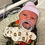 baby, newborn, infant, hat, pacifier, mitten, bear_pattern, camo_clothing, cushion, patterned_bedding, face, person, cute, resting, closeup, indoors, child, pink_hat, orange_text, soft_lighting