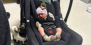 Oakley is registered to the contest to win money with this photo: baby, newborn, car_seat, toy, stuffed_animal, floor, socks, hat, sleeping, infant, person, clothing, indoor, footwear, black_shoe, tile_floor, seat_belt, baby_toy, quiet, resting