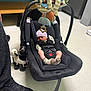 baby, newborn, car_seat, toy, stuffed_animal, floor, socks, hat, sleeping, infant, person, clothing, indoor, footwear, black_shoe, tile_floor, seat_belt, baby_toy, quiet, resting