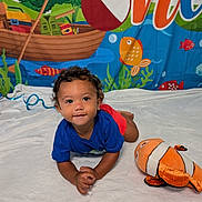 Marcel joined the competition — help win amazing prizes! toddler, child, blue_shirt, red_shorts, curly_hair, smiling, plush_toy, clownfish, white_blanket, underwater_background, colorful_banner, fish, boat, water_splash, indoor, playing, cute, portrait, happy, floor_rug