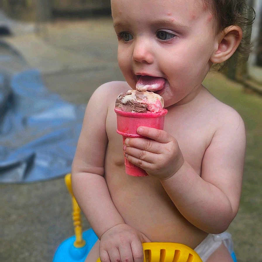 Mariah is registered to the contest to win money with this photo: baby, bodypart, clothing, cream, cutlery, dessert, face, finger, food, head, icecream, icing, outdoors, person, photography, portrait, sitting, spoon, summer, swimwear