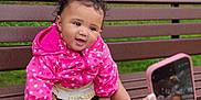 Malaya joined the competition — help win amazing prizes! baby, child, pink_jacket, polka_dots, bench, park, outdoor, smiling, cute, curly_hair, person, photography, smartphone, hands, nature, trees, greenery, sitting, happy, portrait