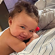 Malaya is registered to the contest to win money with this photo: baby, smile, curly_hair, blanket, striped, lying_down, cheeky, face, skin, indoors, cozy, child, cute, portrait, happy, infant, expression, soft_light, young, person