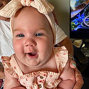 Payton is registered to the contest to win money with this photo: baby, child, smiling, headband, blue_eyes, pink_clothing, adult_hand, nail_polish, indoor, television, furniture, skin, face, person, cute, happy, holding, closeup, infant, portrait