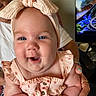 baby, child, smiling, headband, blue_eyes, pink_clothing, adult_hand, nail_polish, indoor, television, furniture, skin, face, person, cute, happy, holding, closeup, infant, portrait