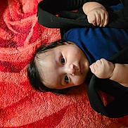 William joined the competition — help win amazing prizes! baby, infant, child, face, hands, clothing, blanket, red, black, pattern, lying_down, portrait, cute, soft, skin, hair, expression, indoor, cozy, curious