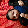 baby, infant, child, face, hands, clothing, blanket, red, black, pattern, lying_down, portrait, cute, soft, skin, hair, expression, indoor, cozy, curious