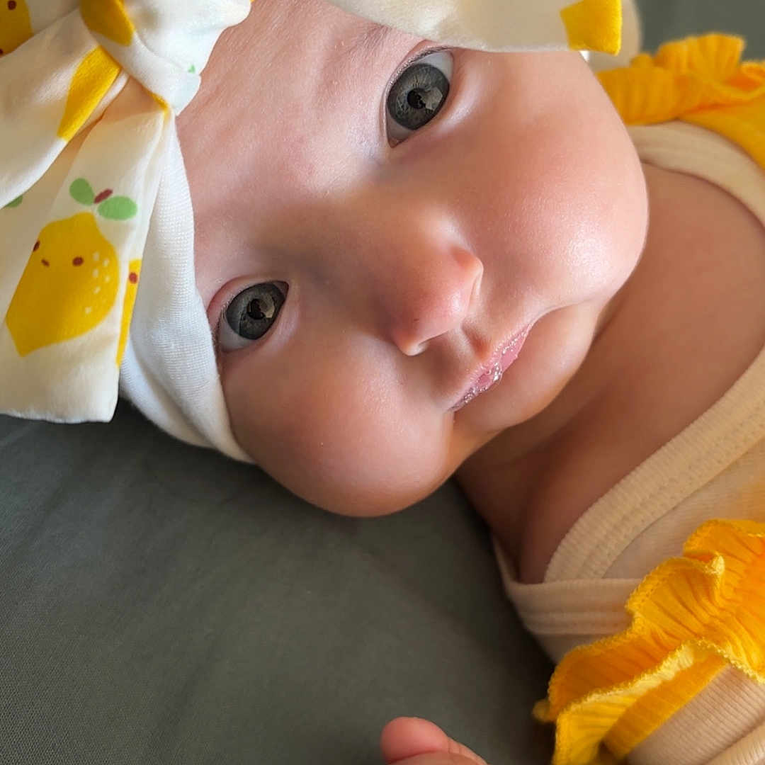 Sowene participe au concours pour gagner de l'argent avec cette photo : adorable, baby, cheeks, child, close_up, clothing, cute, expression, eyes, fabric, fist, headband, indoors, infant, lemon_pattern, lying_down, newborn, portrait, soft_skin, yellow