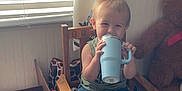 Oakley joined the competition — help win amazing prizes! toddler, child, chair, blue_cup, blanket, pacifier, window, curtain, wooden_furniture, teddy_bear, floor, indoor, smiling, clothing, jeans, green_shirt, toy, cardboard_box, natural_light, home