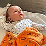 baby, infant, blanket, towel, clothing, face, person, lying_down, indoor, cute, soft_texture, orange_blanket, white_towel, stars_pattern, pajamas, newborn, child, portrait, skin, head