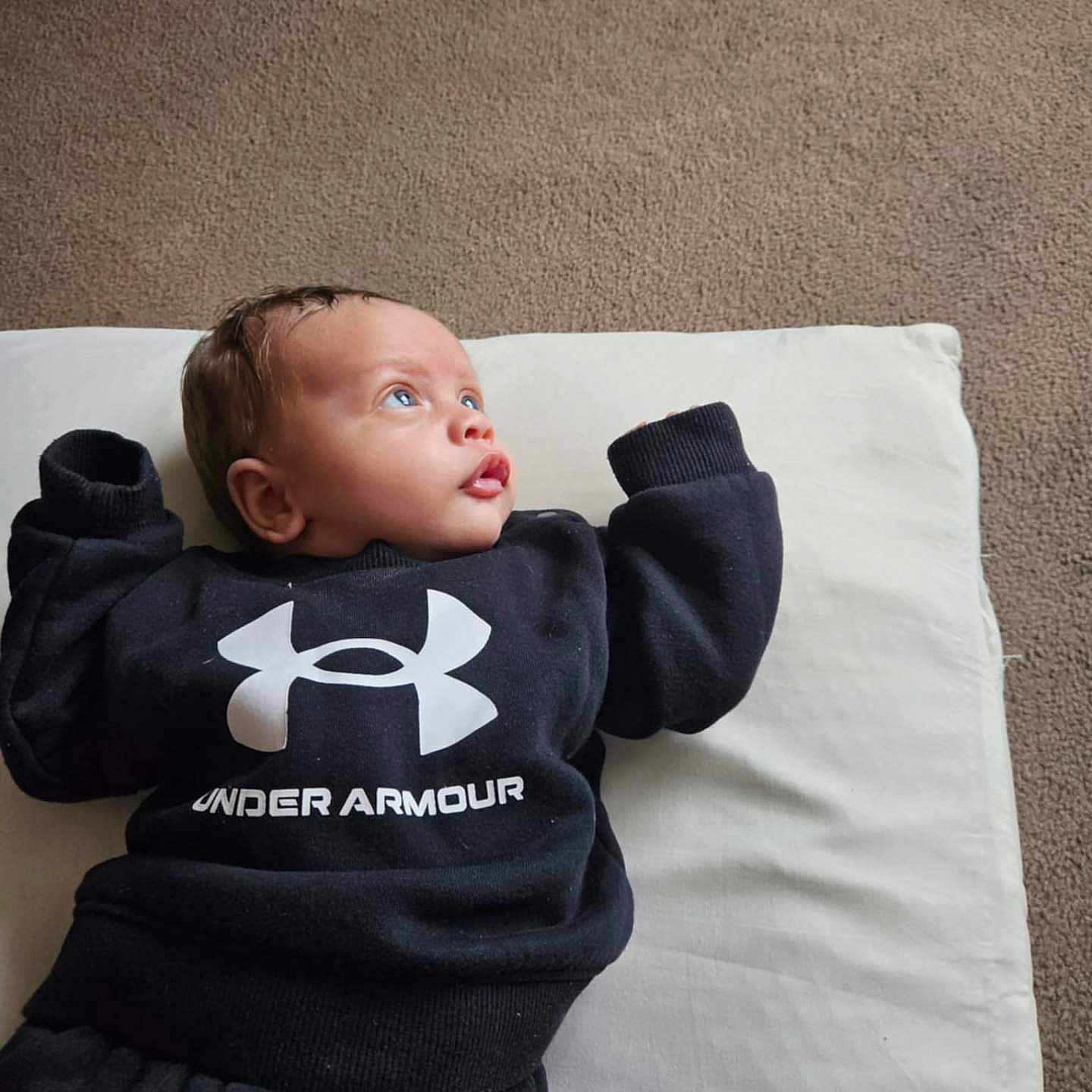 Nwaora is registered to the contest to win money with this photo: baby, black_clothing, blue_eyes, carpet, casual, child, comfortable, cozy, curious, cushion, cute, indoor, infant, lying_down, pants, person, portrait, sweatshirt, under_armour, young