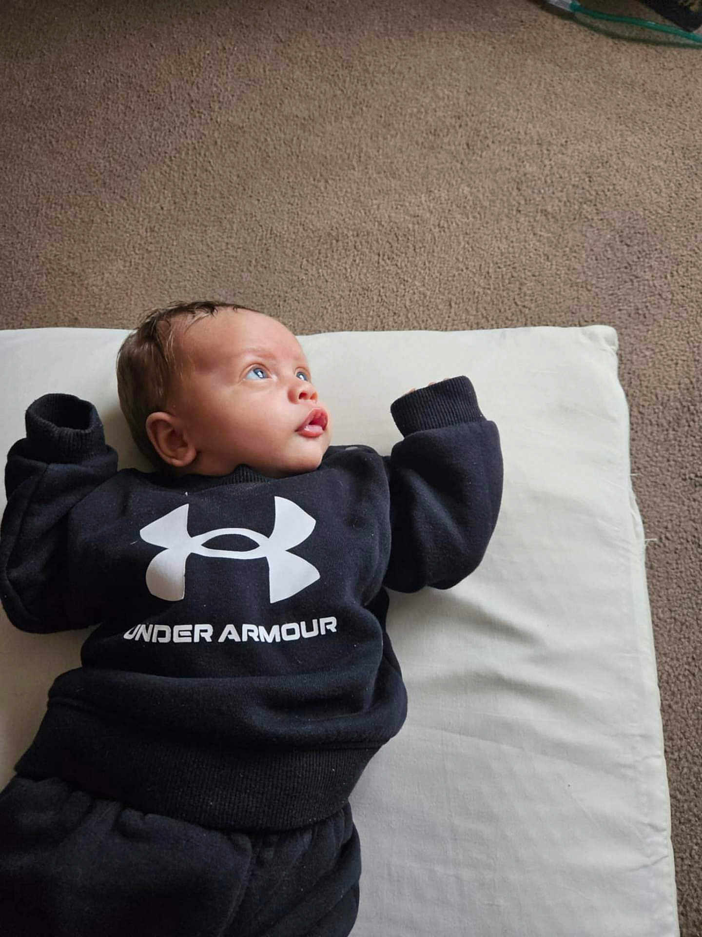 Nwaora is registered to the contest to win money with this photo: baby, infant, under_armour, black_clothing, cushion, carpet, lying_down, blue_eyes, curious, indoor, child, sweatshirt, pants, person, portrait, casual, comfortable, young, cute, cozy