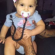 Sunny is registered to the contest to win money with this photo: arm, baby, bow, child, closeup, cute, hand, happy, headband, holding, indoor, infant, lights, pacifier, person, purple, shirt, skin, striped, tattoo