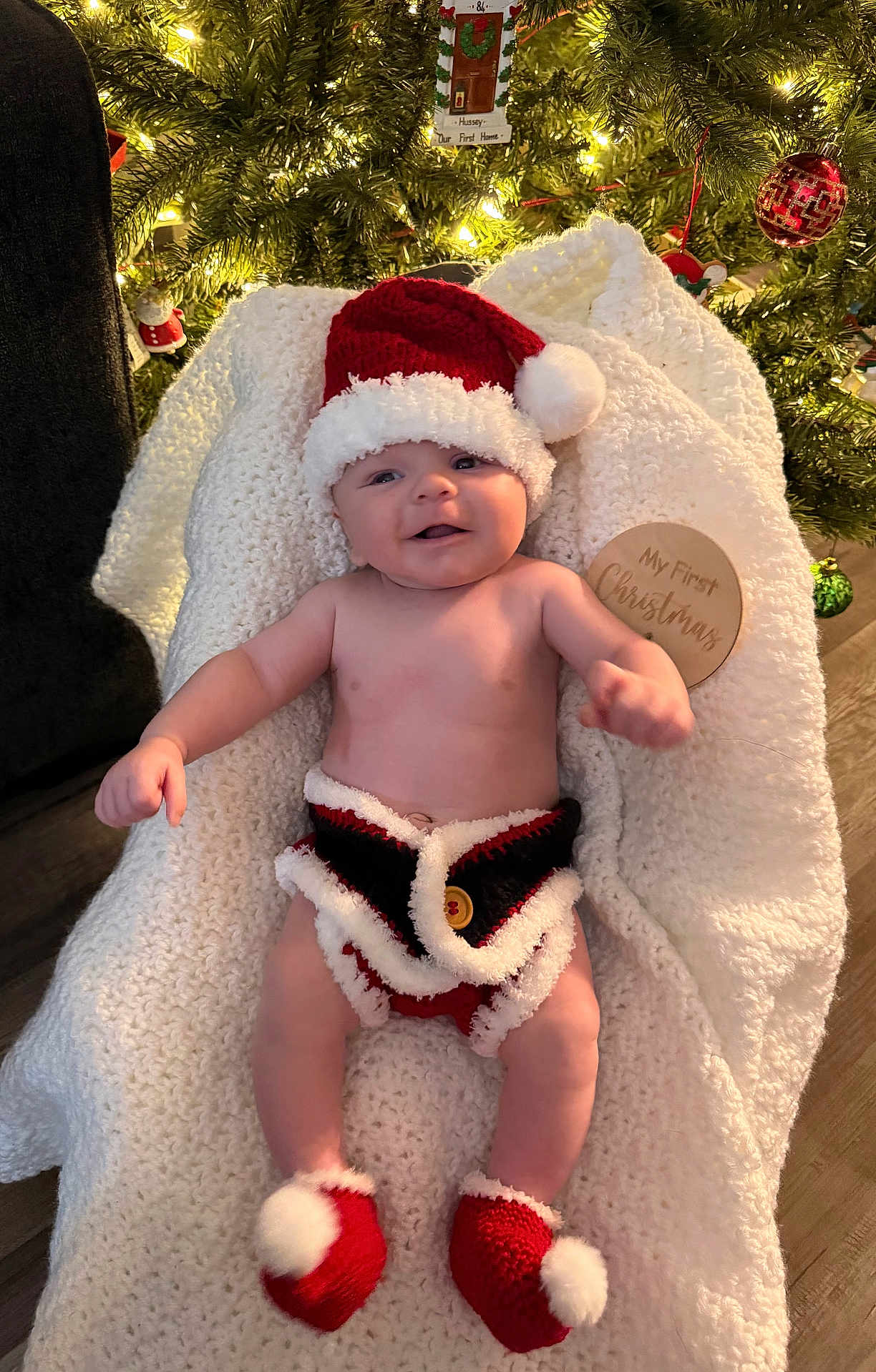 Jameson is registered to the contest to win money with this photo: baby, christmas, holiday, festive, santa_hat, knitwear, blanket, smile, infant, decorations, tree, ornaments, red, white, cozy, cute, indoors, celebration, seasonal, happy