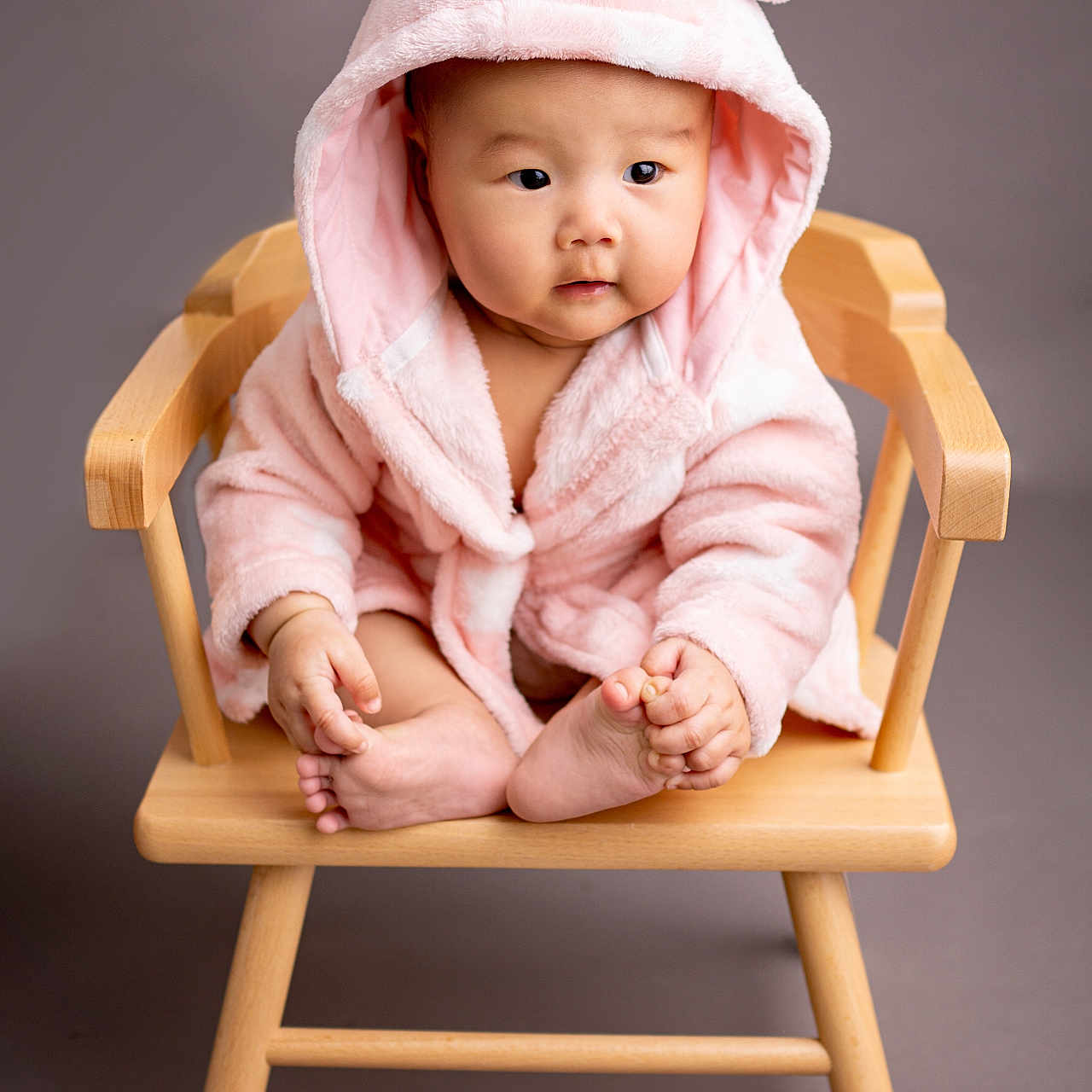 Nuyenma joined the competition — help win amazing prizes! adorable, baby, barefoot, child, child_fashion, cozy, cross_legged, curious_expression, cute, gray_background, hood_with_ears, indoors, infant, pink_robe, portrait, sitting, small_furniture, soft_texture, studio_lighting, wooden_chair