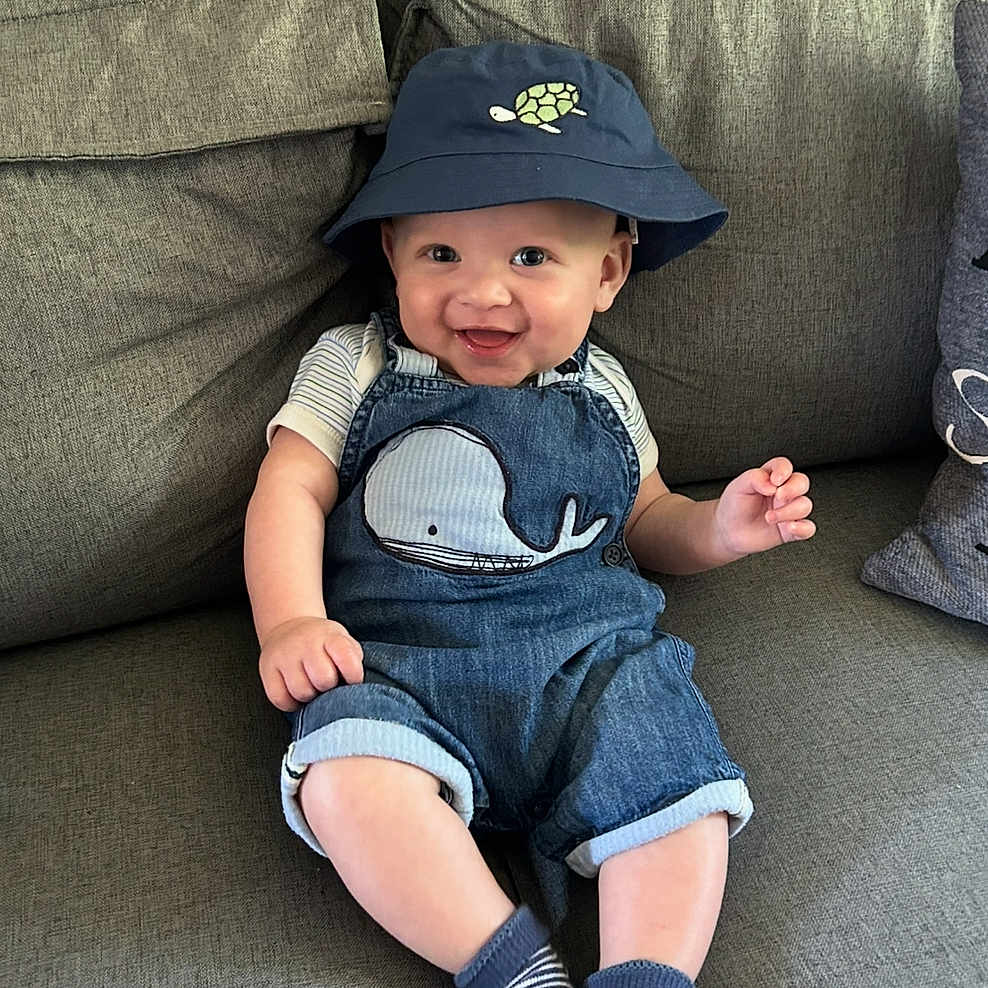 Noah joined the competition — help win amazing prizes! baby, baseballcap, cap, clothing, couch, face, footwear, furniture, hat, head, hosiery, jeans, pants, person, photography, portrait, shoe, shorts, sitting, sock