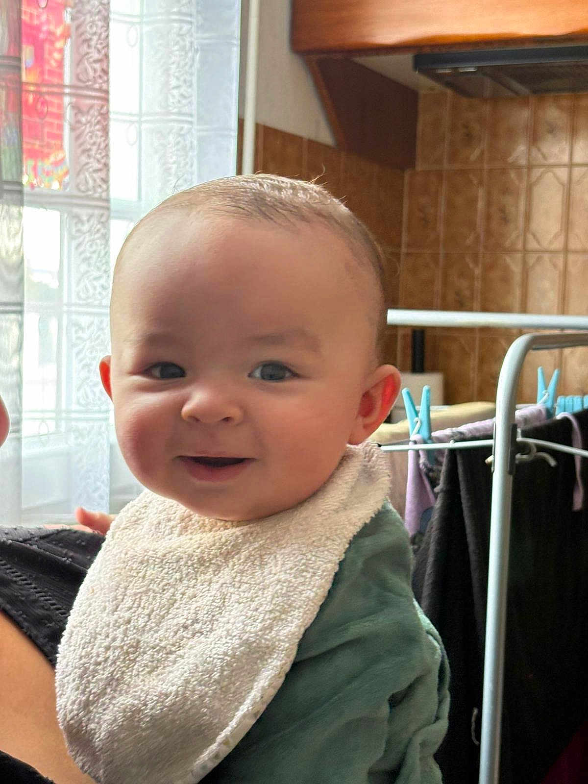 Lylio participe au concours pour gagner de l'argent avec cette photo : baby, smiling, indoor, blanket, bib, face, child, person, window, curtain, clothing, drying_rack, tiled_wall, home, portrait, cute, happy, young_child, fabric, soft