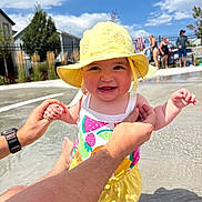 Jensen is registered to the contest to win money with this photo: baby, child, infant, smiling, happy, sunhat, yellow_clothing, swimsuit, outdoor, pool, swimming_pool, water, summer, sunny, family, adult_hands, portrait, playful, residential_background, blue_sky