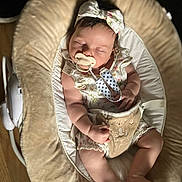 Lilith is registered to the contest to win money with this photo: baby, sleeping, pacifier, headband, baby_rocker, cushion, infant, clothing, hand, foot, wooden_floor, comfort, peaceful, cute, soft_light, indoor, child, adorable, plush, resting