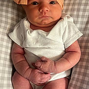 Elizabeth is registered to the contest to win money with this photo: baby, infant, headband, bow, white_onesie, pillow, checkered_pattern, hands, legs, skin, face, eyes, indoor, newborn, cute, resting, clothing, soft_light, portrait, child