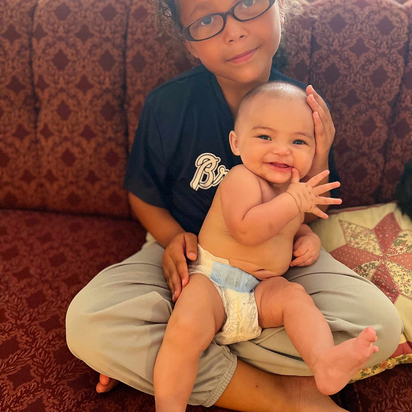 Joseph is registered to the contest to win money with this photo: accessories, baby, clothing, couch, cushion, diaper, face, furniture, glasses, happy, head, homedecor, newborn, people, person, photography, portrait, sitting, smile, t_shirt