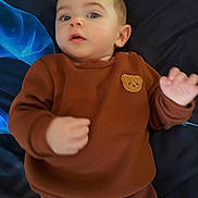 Mathias a rejoint le concours — aidez-le/la à gagner de superbes lots ! baby, child, infant, brown_clothing, teddy_bear_patch, blue_background, lying_down, hand, face, eyes, portrait, cute, young_child, sleeve, sweater, casual_wear, person, indoor, soft_lighting, expression