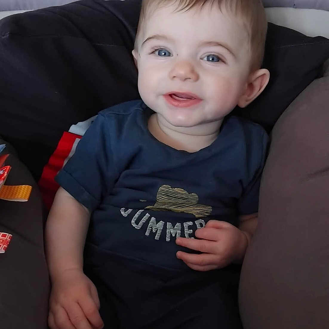 Mathias a rejoint le concours — aidez-le/la à gagner de superbes lots ! baby, child, smiling, blue_eyes, cushion, seat, navy_shirt, summer_graphic, indoor, portrait, cute, happy, infant, person, clothing, shorts, skin, hand, face, hair
